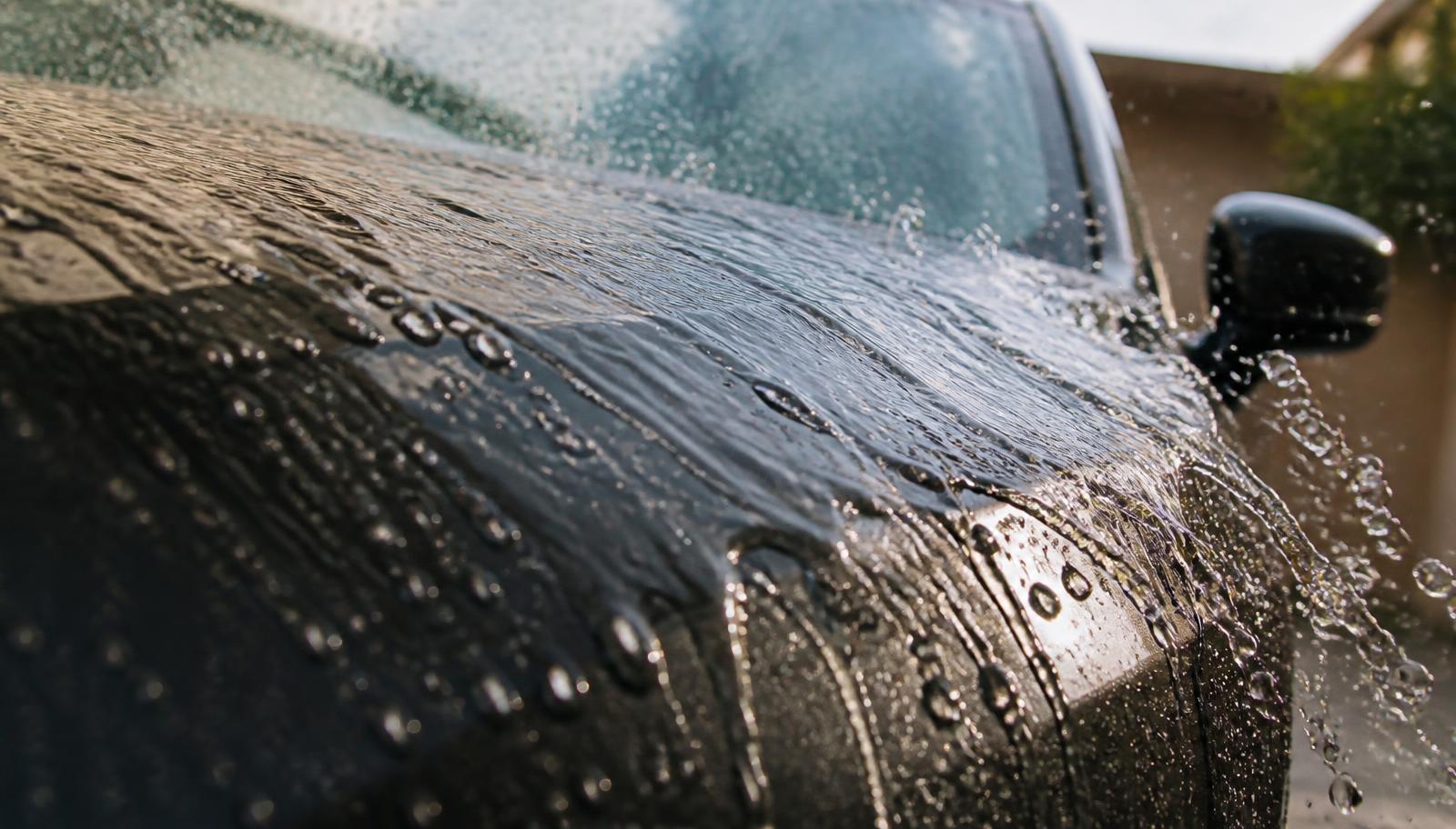 Water sheeting off the glossy paint of a dark vehicle during rinse