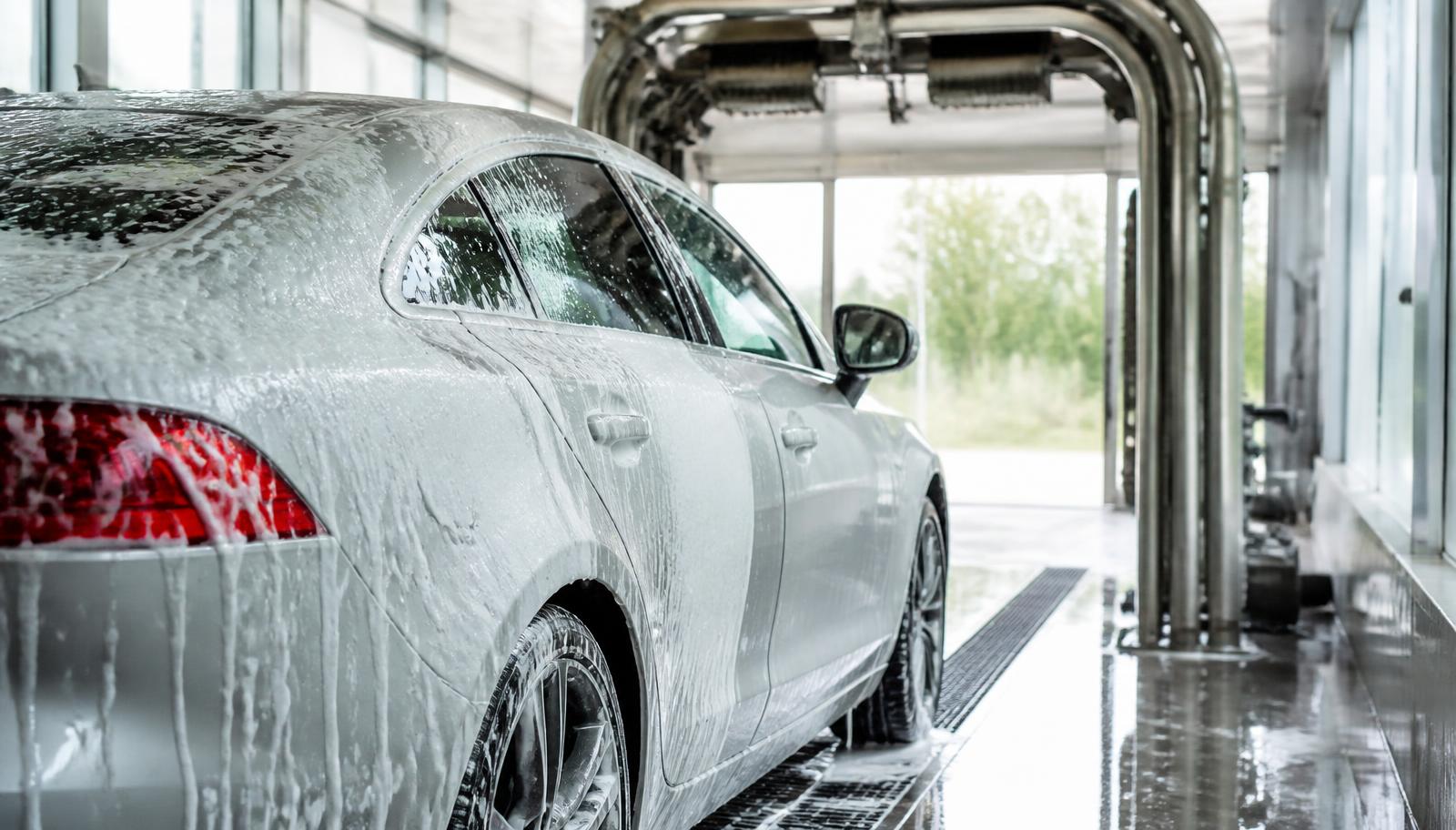 A car covered in wash foam moving through a bright wash tunnel